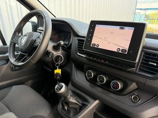 Vue intérieure côté conducteur du Renault Trafic Combi gris comète, avec volant, levier de vitesses manuel et écran tactile affichant la navigation.