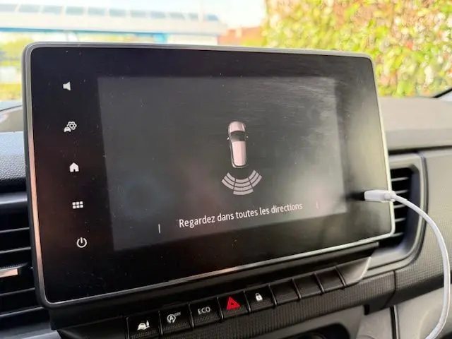 Écran tactile central du Renault Trafic Combi gris comète, affichant l'alerte de surveillance des angles morts.