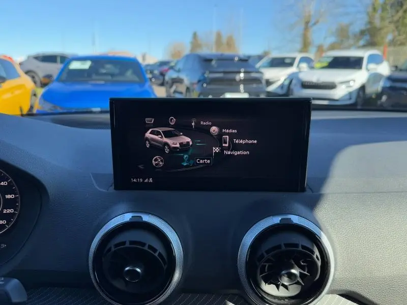 Écran central de l'Audi Q2 2024 affichant le menu multimédia, avec aérateurs ronds et tableau de bord noir.