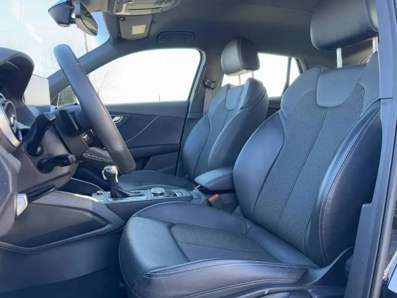 Vue intérieure côté conducteur de l'Audi Q2 30 TDI S line 2024 avec sièges sport noirs et volant cuir multifonction.