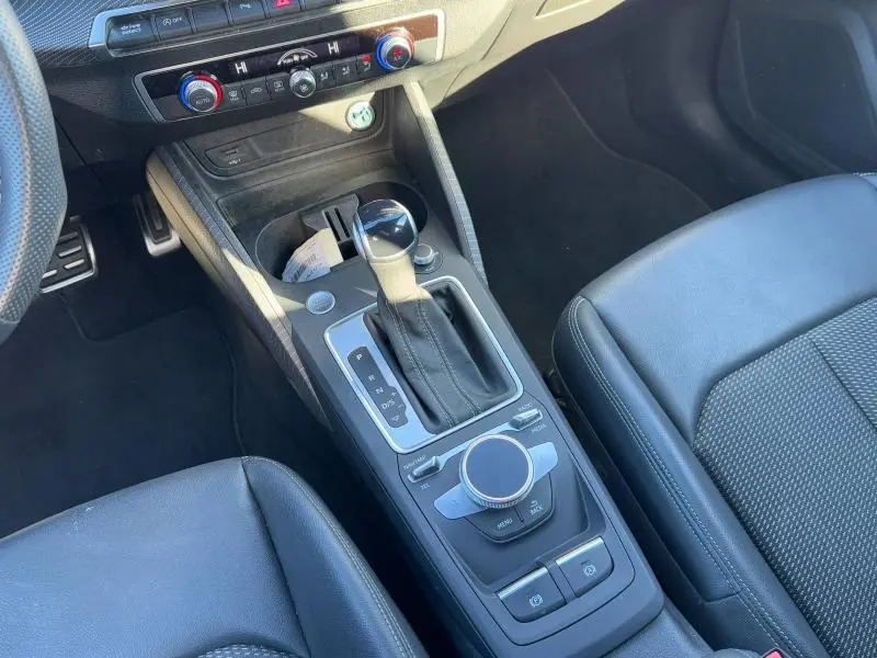 Vue rapprochée de la console centrale noire de l'Audi Q2 30 TDI 2024 avec levier de vitesse automatique et commandes multimédia.