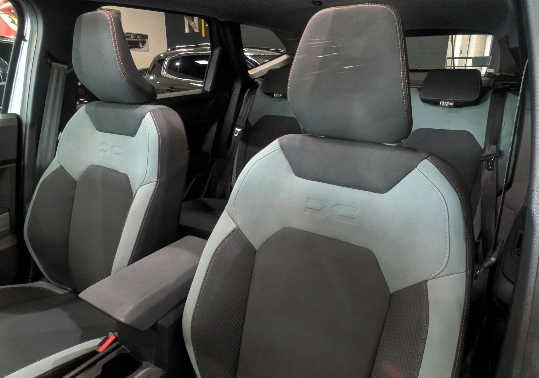 Vue intérieure rapprochée des sièges avant en tissu gris clair et foncé du Dacia Bigster Mild Hybrid 2026, avec surpiqûres rouges.