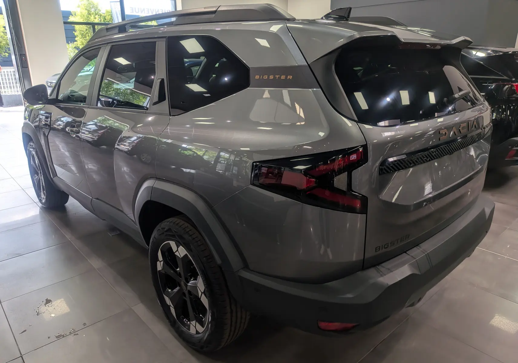 Vue 3/4 arrière droite du Dacia Bigster gris schiste avec jantes noires et logo "Bigster" sur la custode.