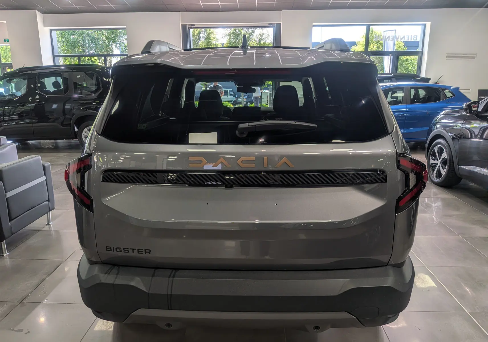 Vue arrière du Dacia Bigster gris schiste en showroom, avec logo Dacia lumineux et feux arrière en forme de C.