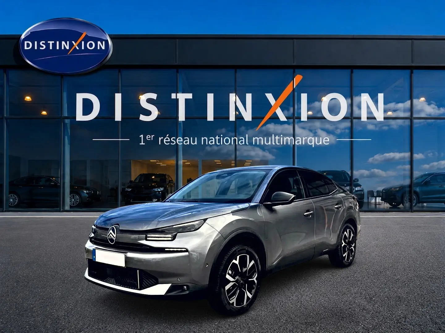 Citroën C4 X gris mercure en 3/4 avant droit, avec jantes alu et calandre distinctive, devant un showroom Distinxion.