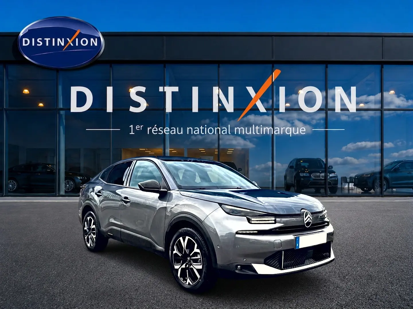 Citroën C4 X gris mercure en 3/4 avant droit, avec jantes alu et calandre distinctive devant un showroom Distinxion.