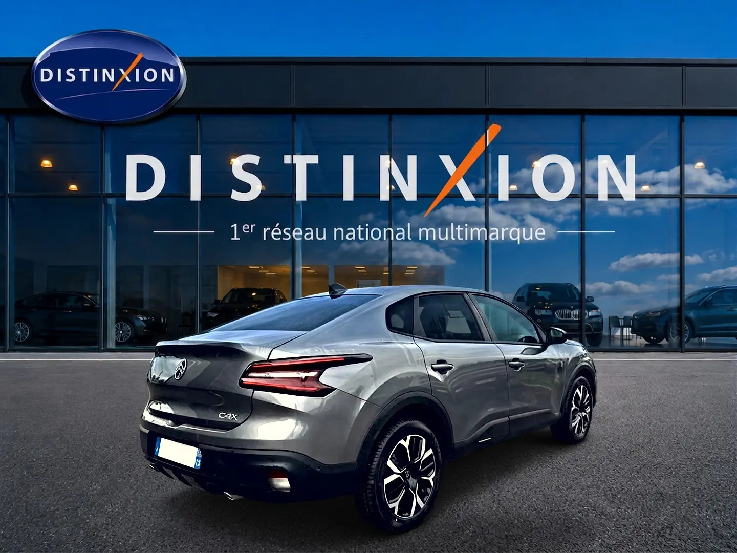Vue 3/4 arrière droite d'une Citroën C4 X gris mercure avec feux LED et jantes alliage devant un showroom Distinxion.