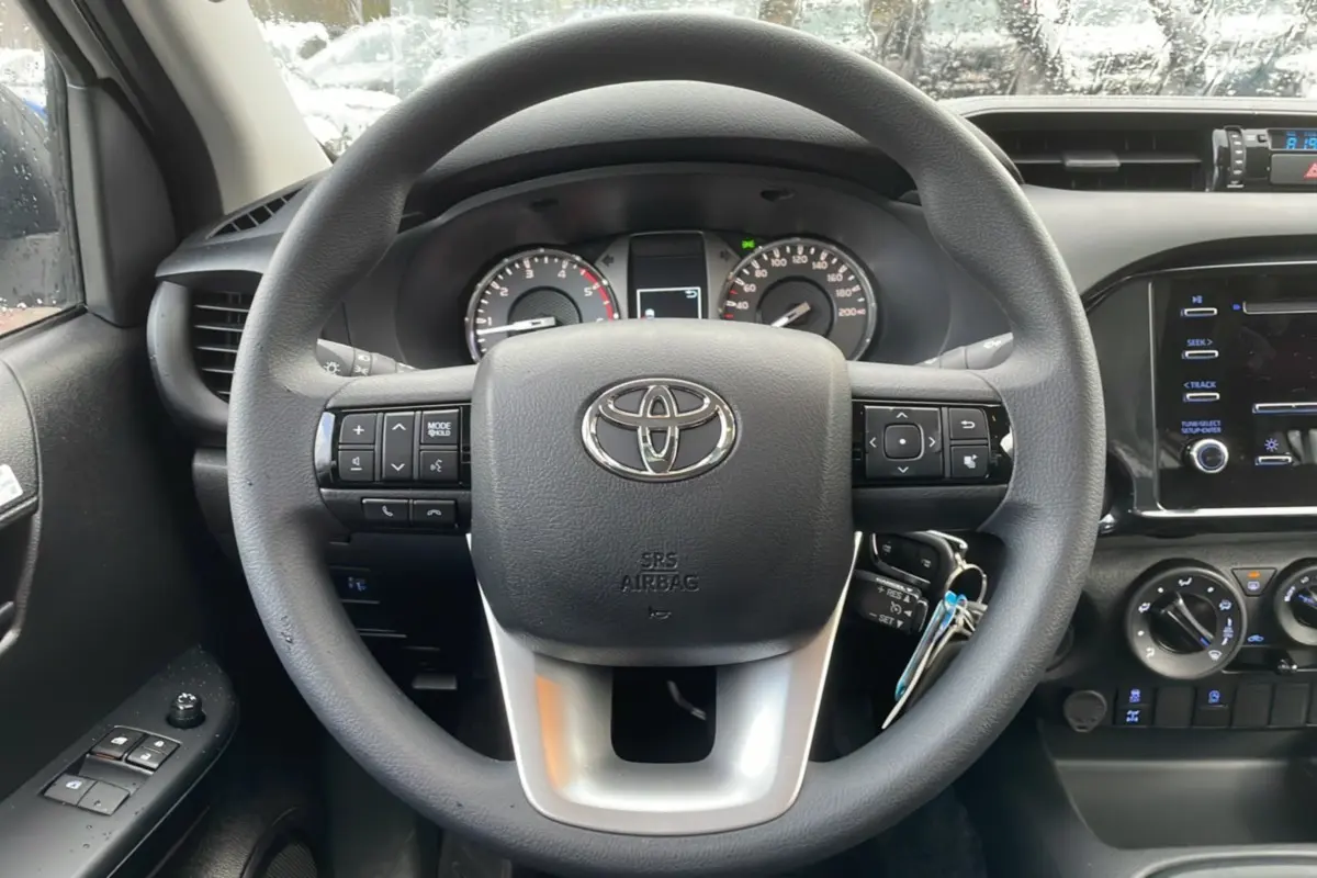 Vue intérieure centrée sur le volant du Toyota Hilux 4x4 2024 avec commandes intégrées et tableau de bord noir.