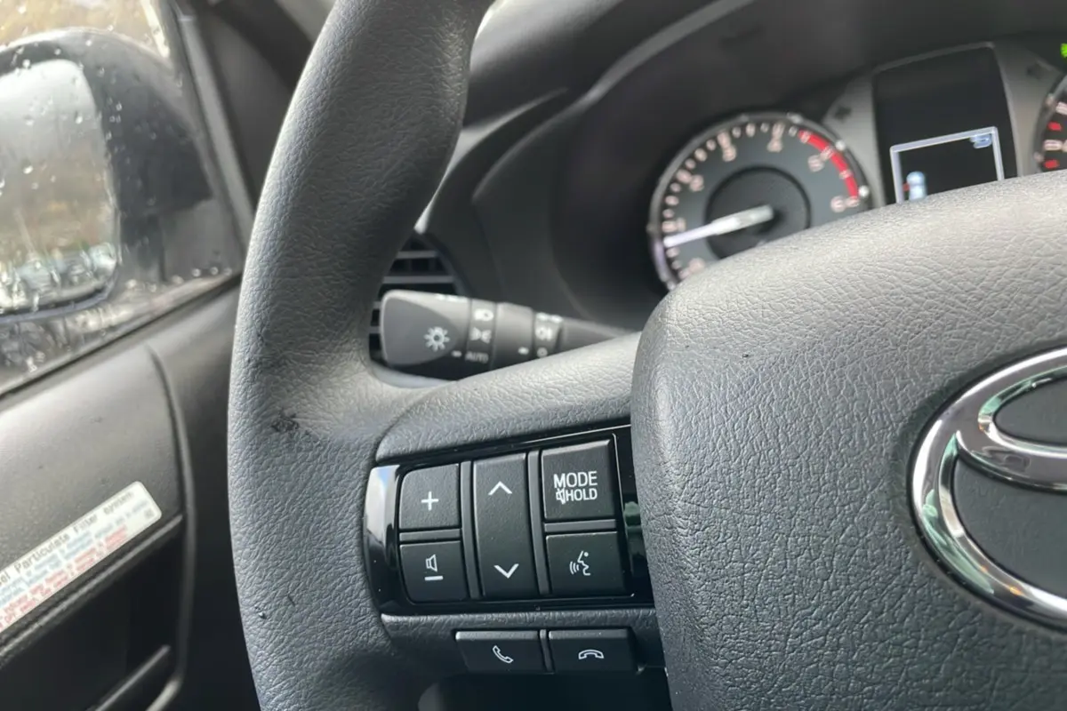 Gros plan sur le volant noir du Toyota Hilux 4x4 2024, avec commandes audio et logo Toyota visible.