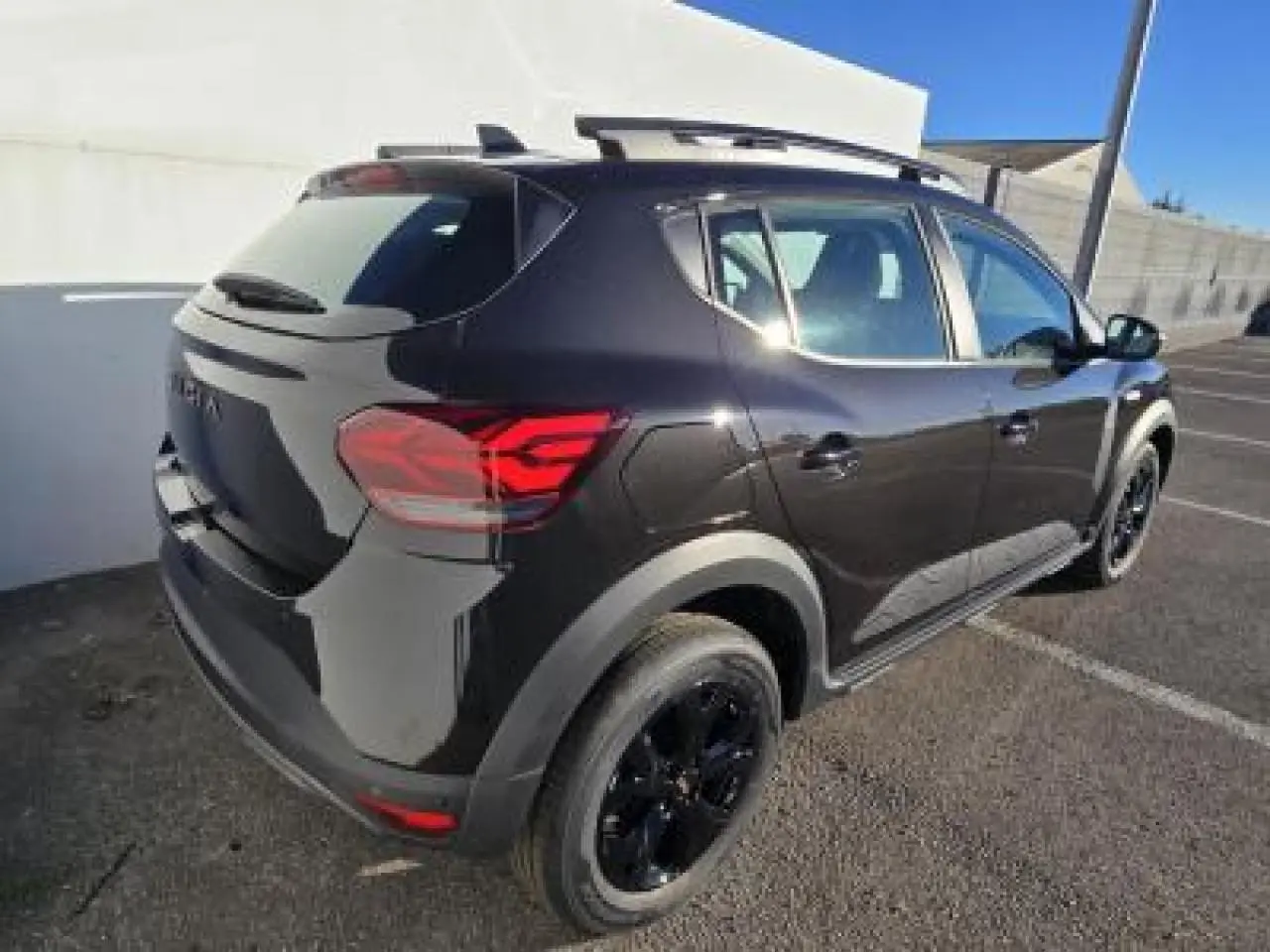 Vue 3/4 arrière droite d'une Dacia Sandero Stepway 2025 noir nacré avec jantes noires et barres de toit
