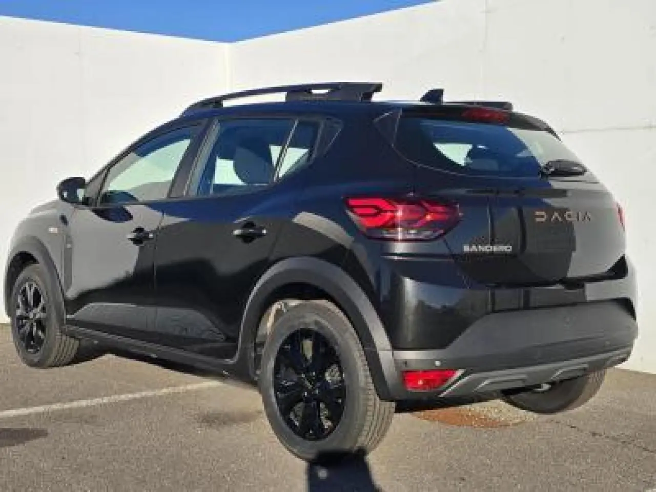 Vue 3/4 arrière droite d'une Dacia Sandero III Stepway noir nacré avec jantes noires et barres de toit visibles