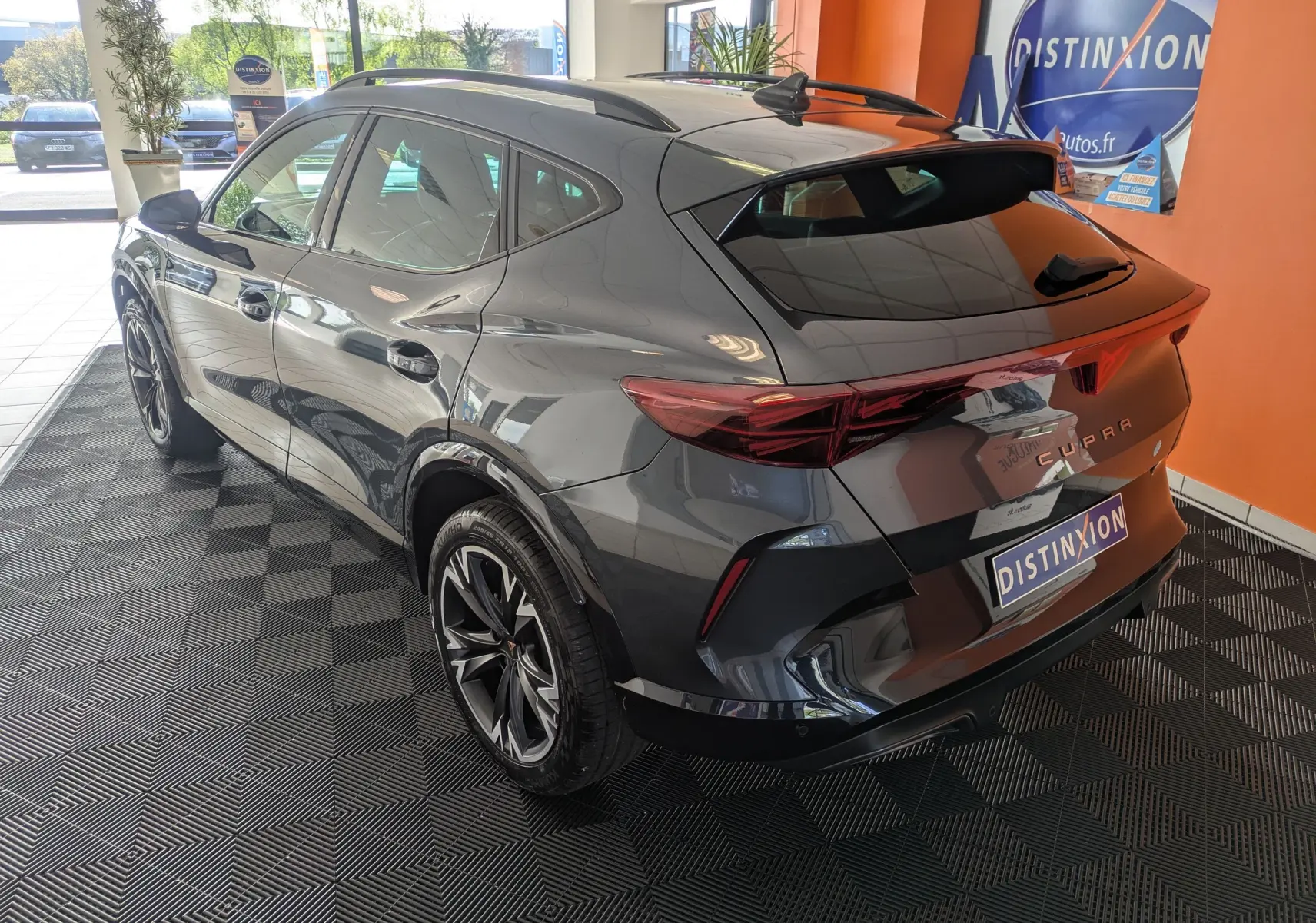 Vue 3/4 arrière droite du CUPRA Formentor gris magnétique avec jantes alliage 18'' bicolores et hayon électrique en intérieur showroom.