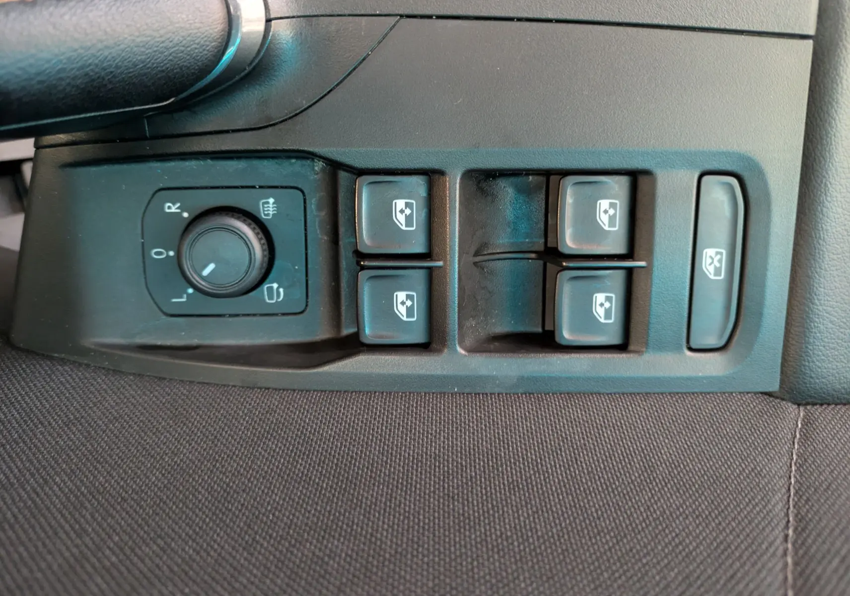 Gros plan sur les commandes de réglage des rétroviseurs et des vitres électriques côté conducteur, intérieur noir.