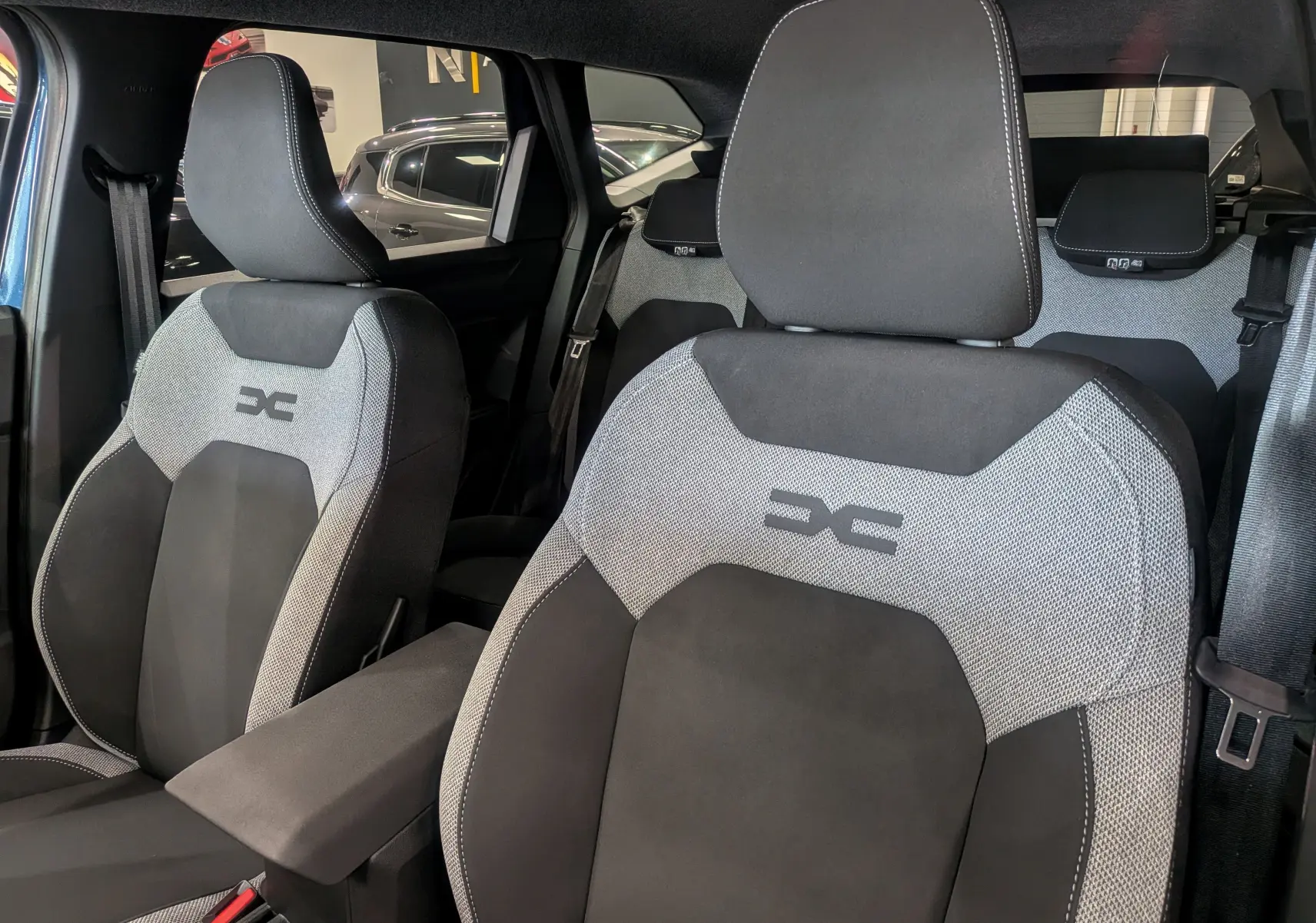 Gros plan sur les sièges avant tissu gris et noir du Dacia Bigster 2026, mettant en valeur le logo brodé sur les appuie-têtes.