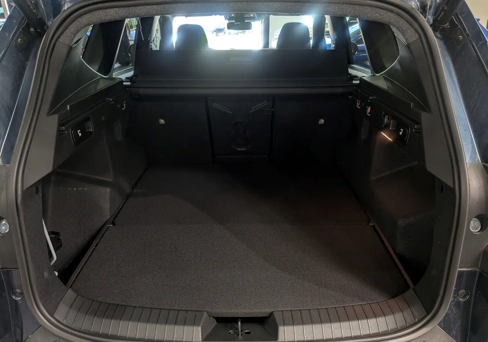 Coffre ouvert du Dacia Bigster bleu indigo, vue arrière montrant un espace de chargement spacieux et bien éclairé.