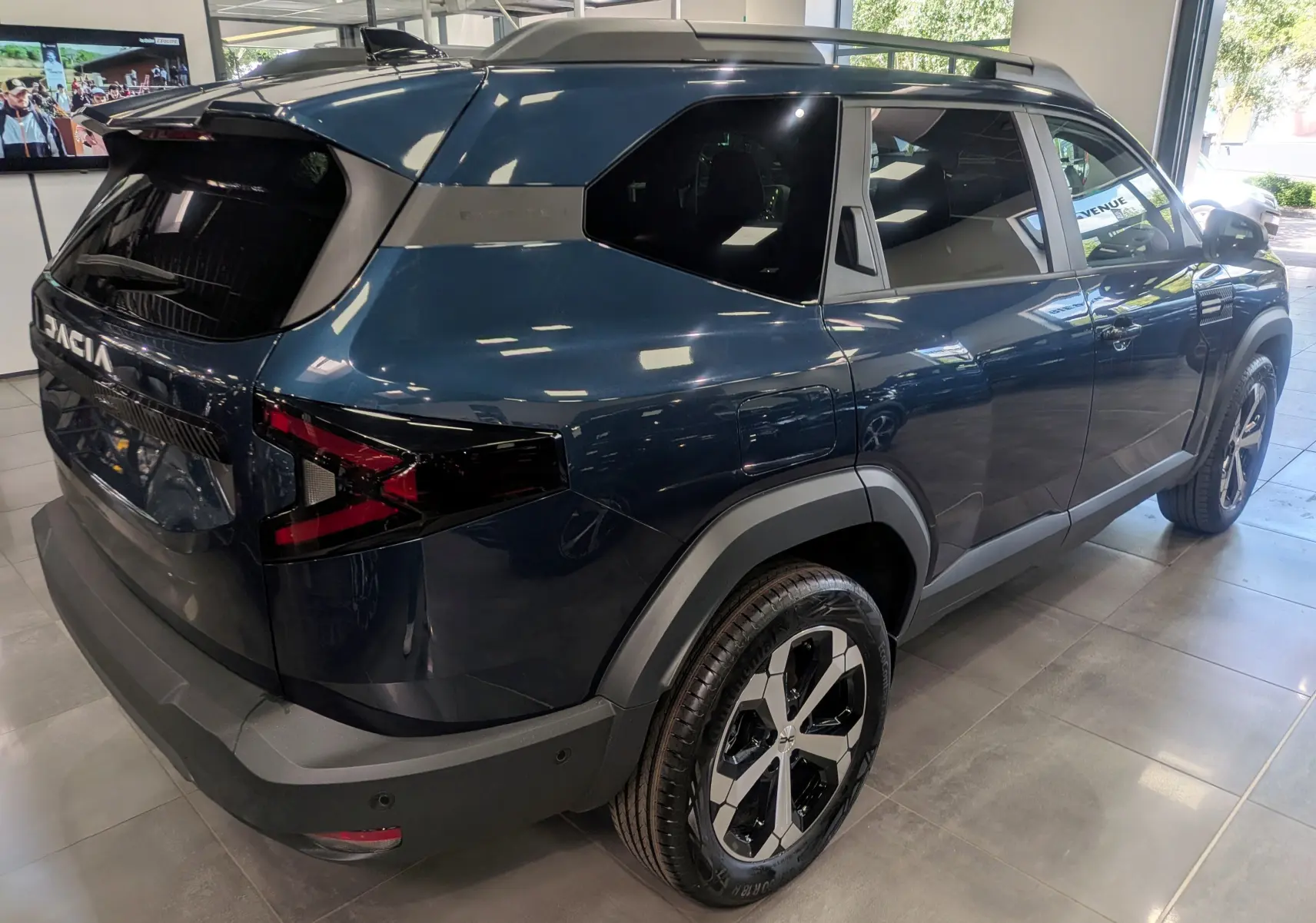 Vue 3/4 arrière droite du Dacia Bigster bleu indigo avec jantes bicolores et vitres teintées en showroom.