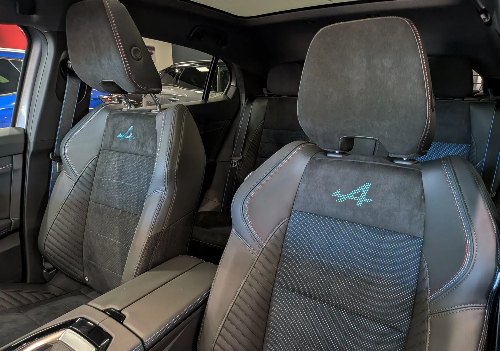 Vue intérieure rapprochée des sièges avant en cuir noir et alcantara avec logo Alpine bleu sur les appuie-têtes.