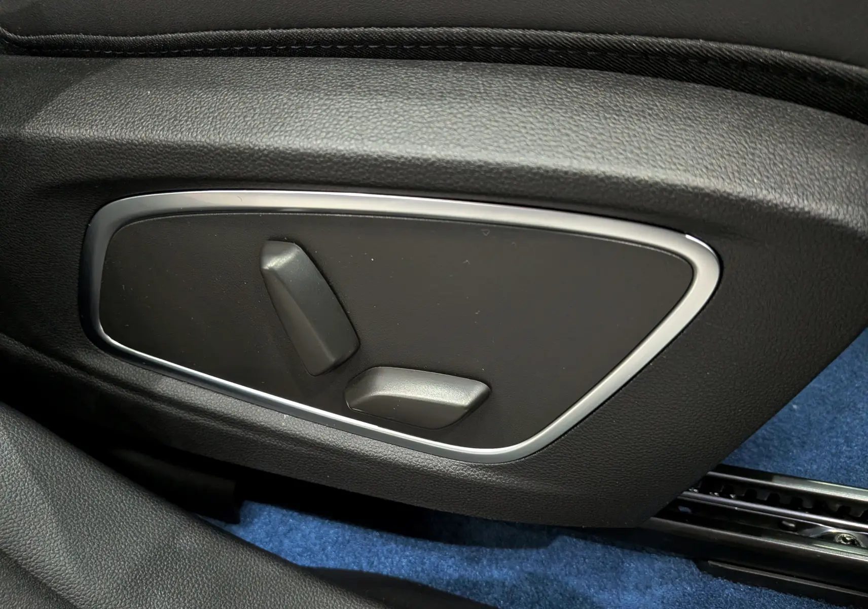 Détail des commandes de réglage électrique du siège côté gauche, intérieur noir avec moquette bleue.