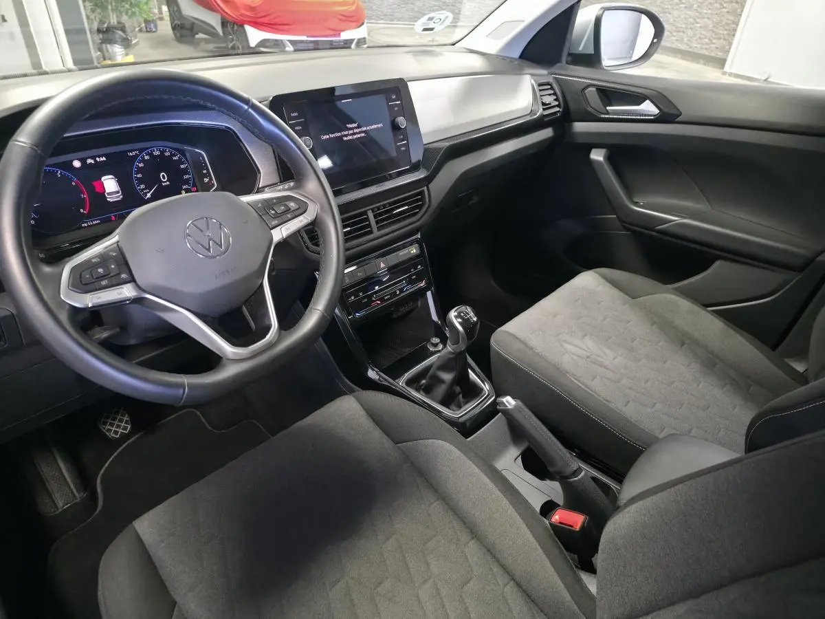 Vue intérieure côté conducteur du Volkswagen T-Cross 1.0 TSI 2025, avec volant cuir, tableau de bord digital et sellerie tissu gris.