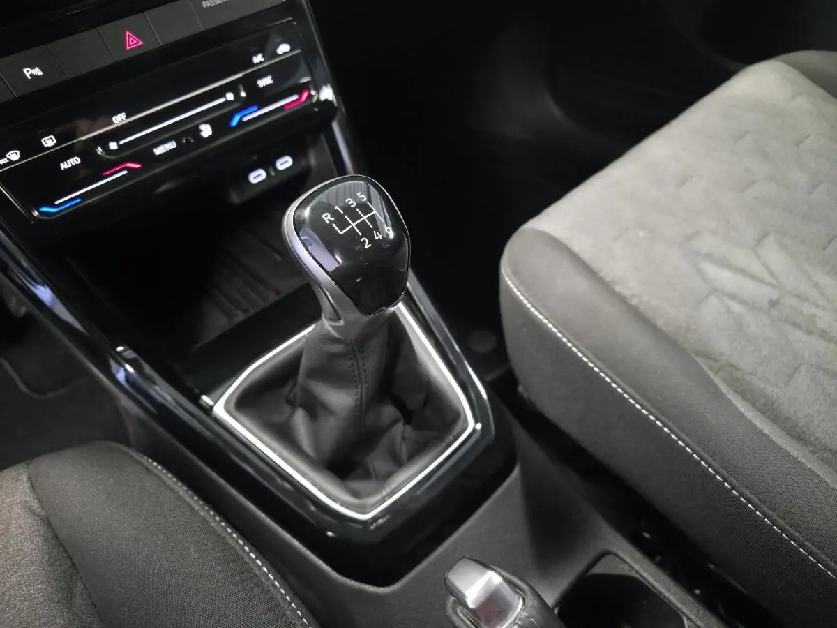 Gros plan sur le levier de vitesses manuel noir et la console centrale du Volkswagen T-Cross gris, siège tissu visible.
