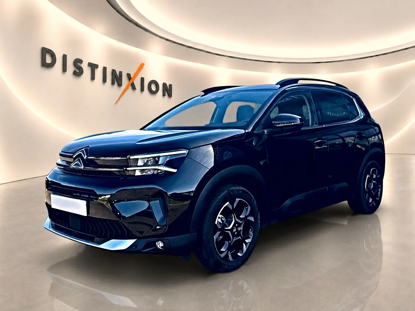 Citroën C5 Aircross noir en 3/4 avant droit, avec barres de toit et jantes alu distinctives dans un showroom lumineux.