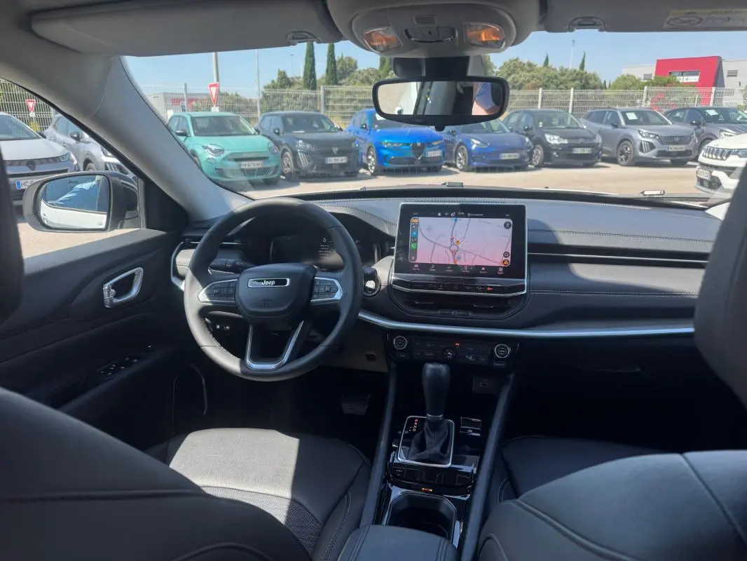 Vue intérieure avant du Jeep Compass 2025 avec tableau de bord noir, écran tactile central et volant multifonction.