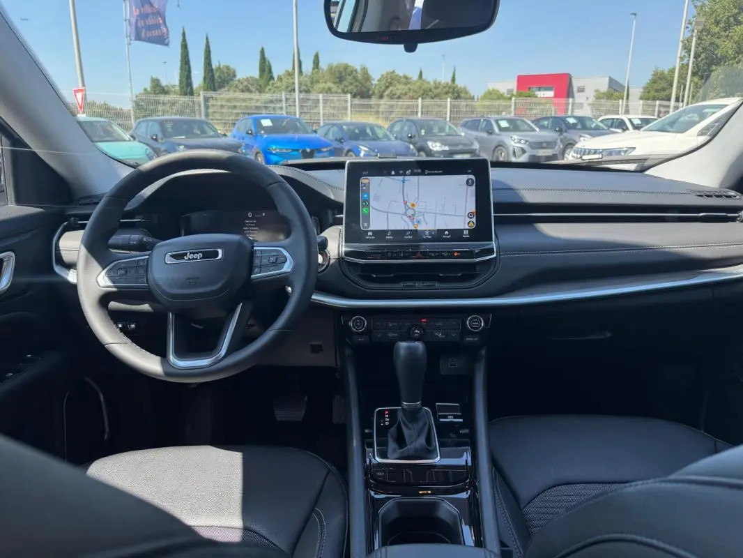 Vue intérieure avant du Jeep Compass 2025 blanc, montrant le volant, écran tactile central et levier de vitesses automatique.