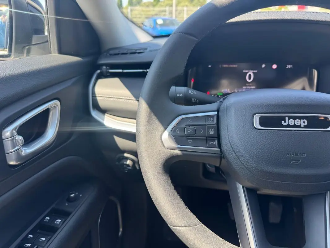 Vue intérieure côté conducteur du Jeep Compass blanc 2025, volant multifonctions et tableau de bord numérique visibles.