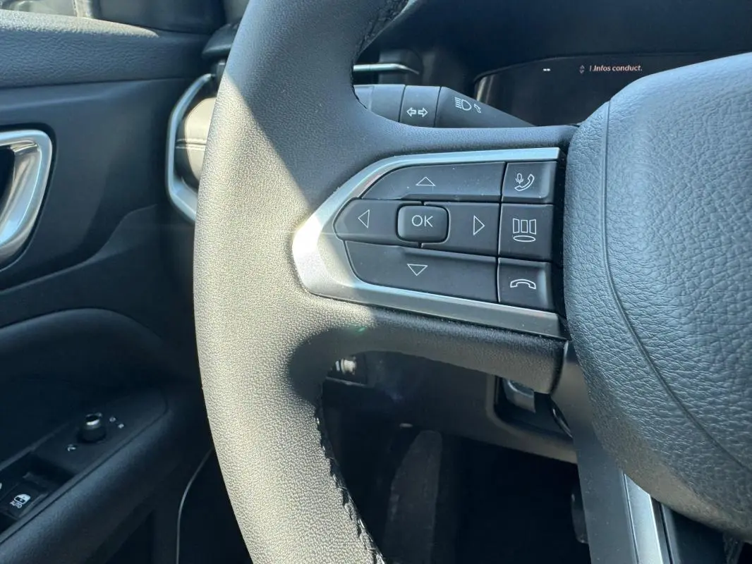 Gros plan sur les commandes à gauche du volant noir du Jeep Compass blanc, avec bouton OK et commandes vocales.