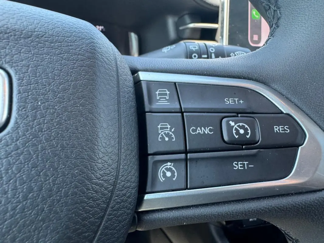 Gros plan sur les commandes du régulateur de vitesse au volant noir du Jeep Compass blanc 2025.