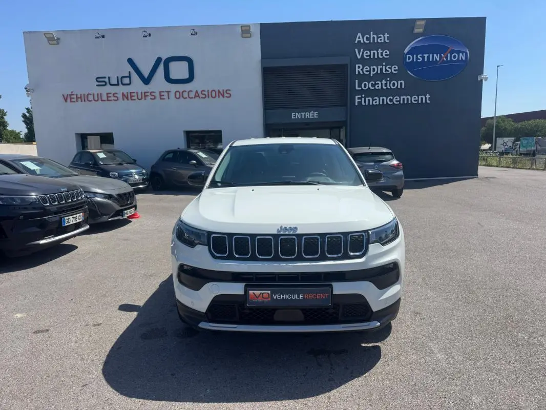 Vue avant d'un Jeep Compass blanc 2025 garé devant un concessionnaire avec calandre distinctive à sept fentes.