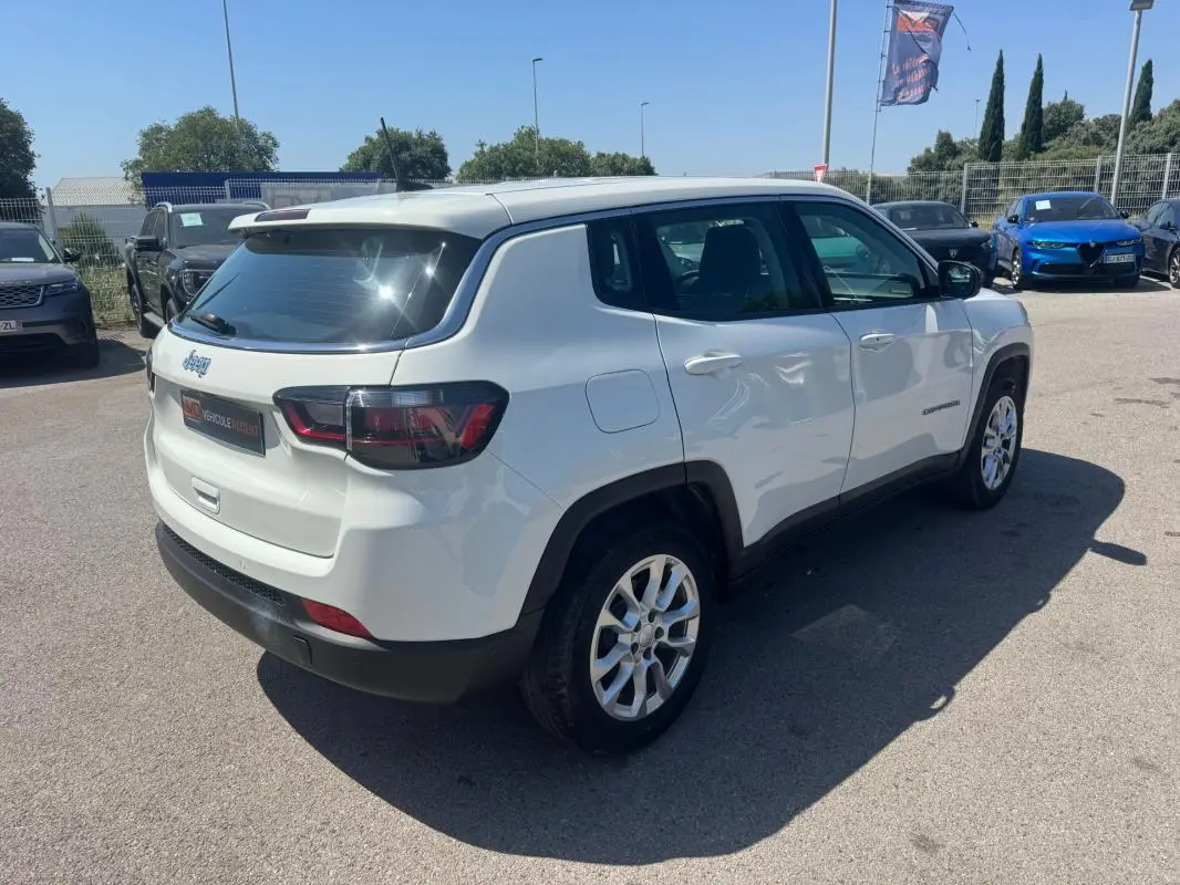 Jeep Compass blanc en vue 3/4 arrière droit, avec jantes alliage et vitres teintées, stationné en extérieur.