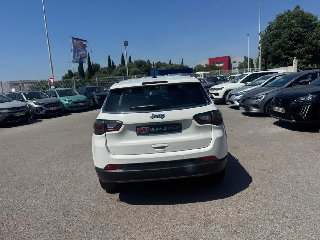 Vue arrière d'un Jeep Compass blanc 2025 garé en extérieur, avec feux arrière sombres et logo Jeep visible.