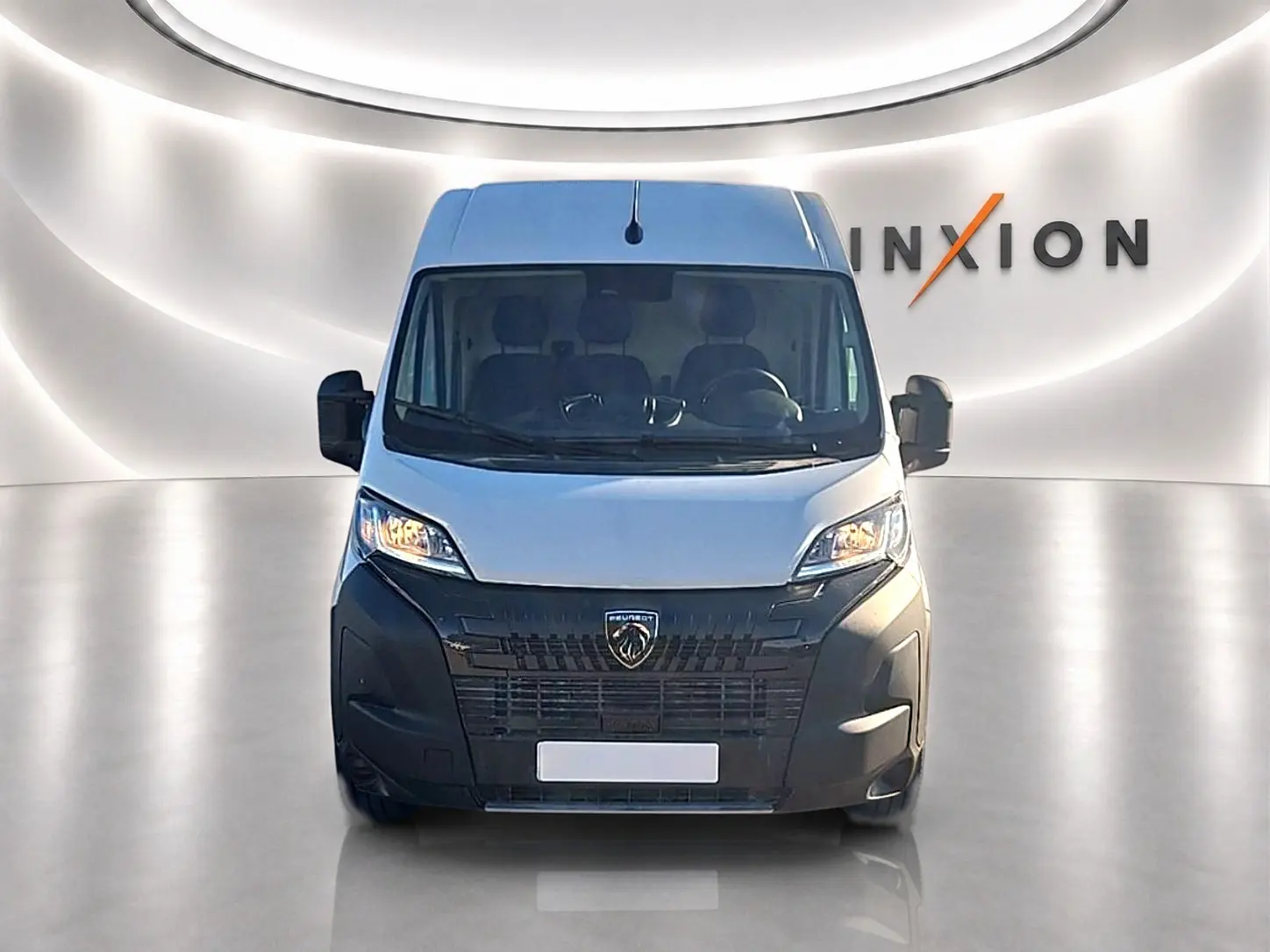 Vue de face du Peugeot Boxer Fourgon blanc avec large calandre noire et phares allumés dans un studio lumineux.