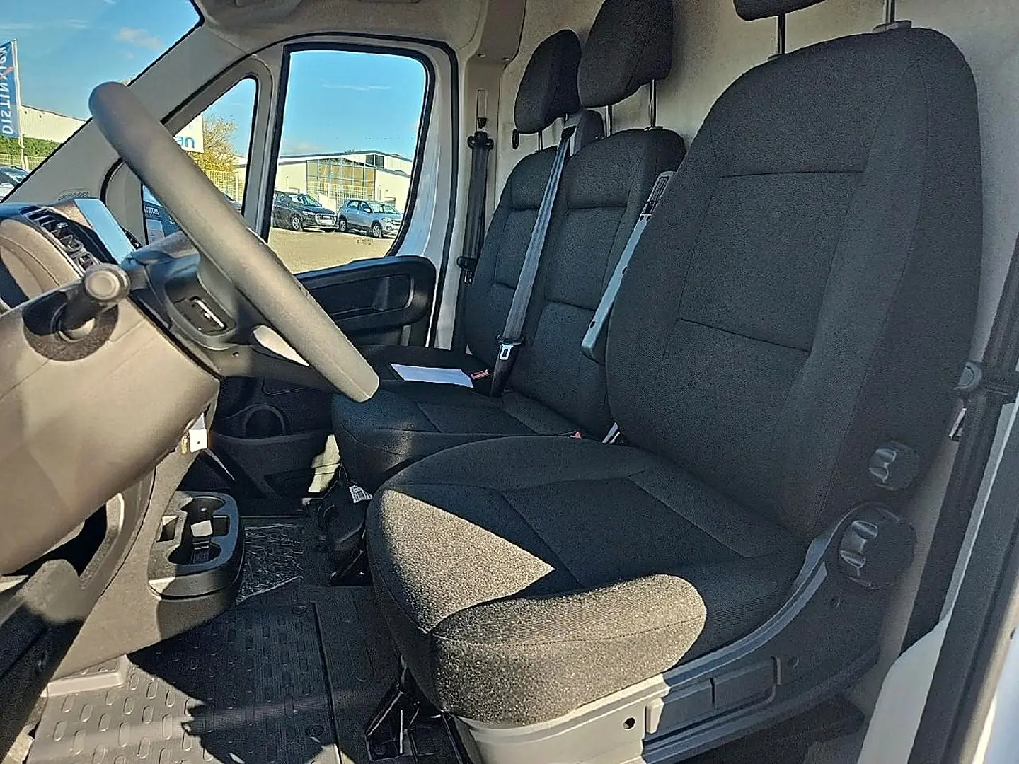 Vue intérieure côté conducteur du Peugeot Boxer Fourgon blanc, montrant la banquette avant noire et le volant.