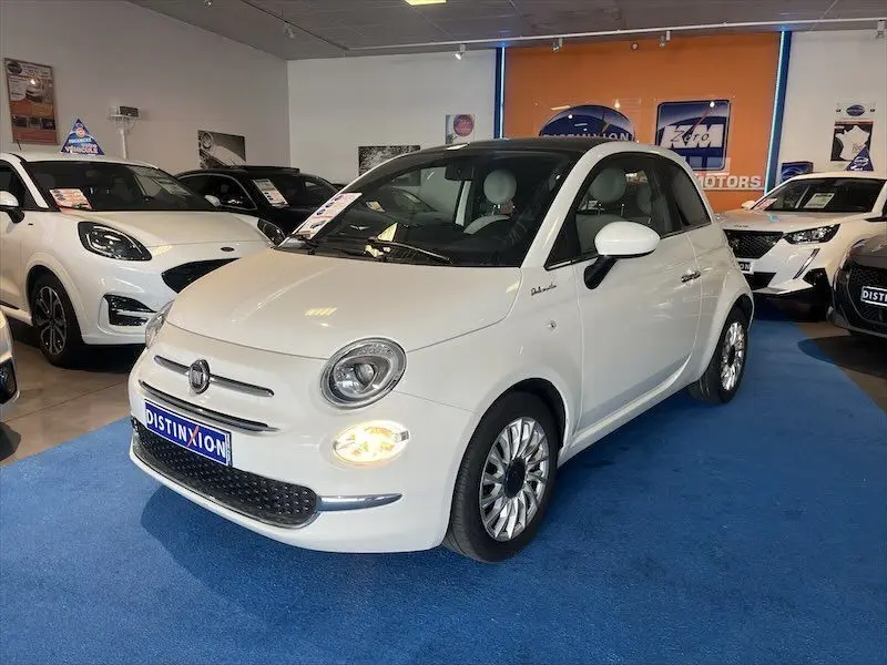 Fiat 500 blanche vue 3/4 avant droit en showroom, phare avant droit allumé et toit noir contrastant.