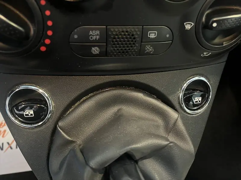 Gros plan sur la console centrale de la Fiat 500 blanche, montrant les commandes des vitres électriques et la commande de climatisation.