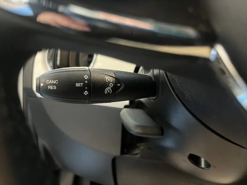 Gros plan sur la commande de régulateur de vitesse noire dans l'habitacle d'une Fiat 500 blanche de 2021.
