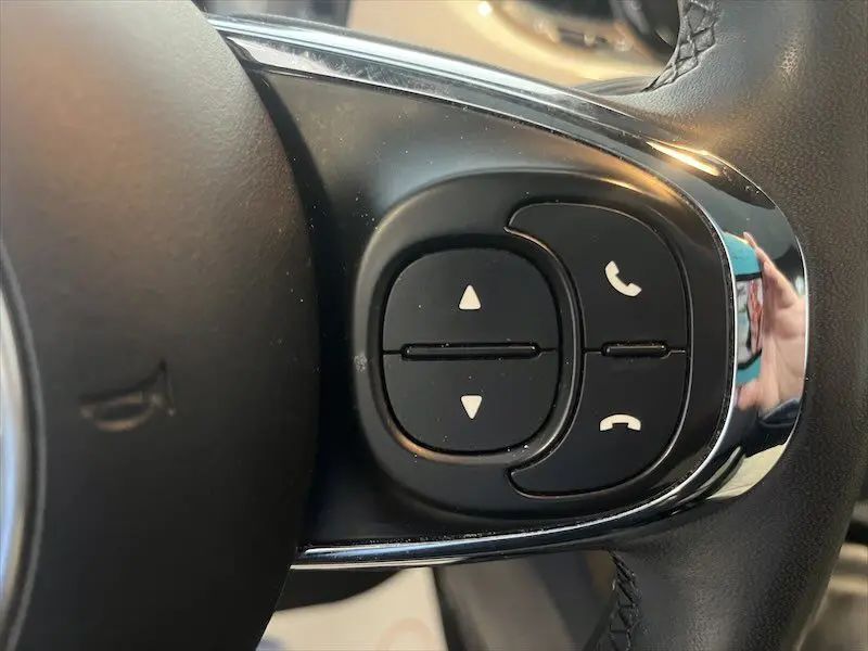 Gros plan sur les commandes noires du volant d'une Fiat 500 blanche, avec boutons de téléphone et navigation.
