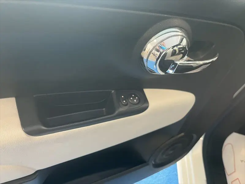 Poignée de porte intérieure côté gauche de la Fiat 500 blanche, avec commandes de vitres et garniture bicolore noir et blanc.