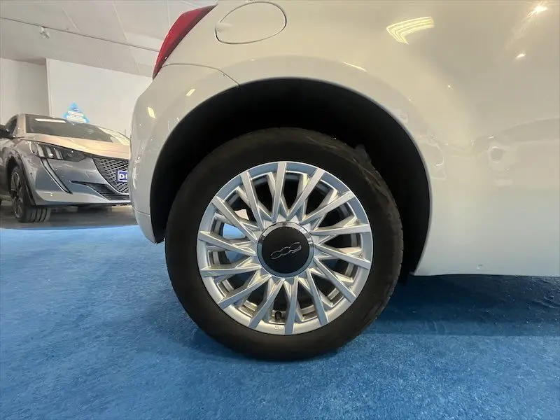 Gros plan sur la roue arrière droite d'une FIAT 500 blanche avec jante argentée en étoile.