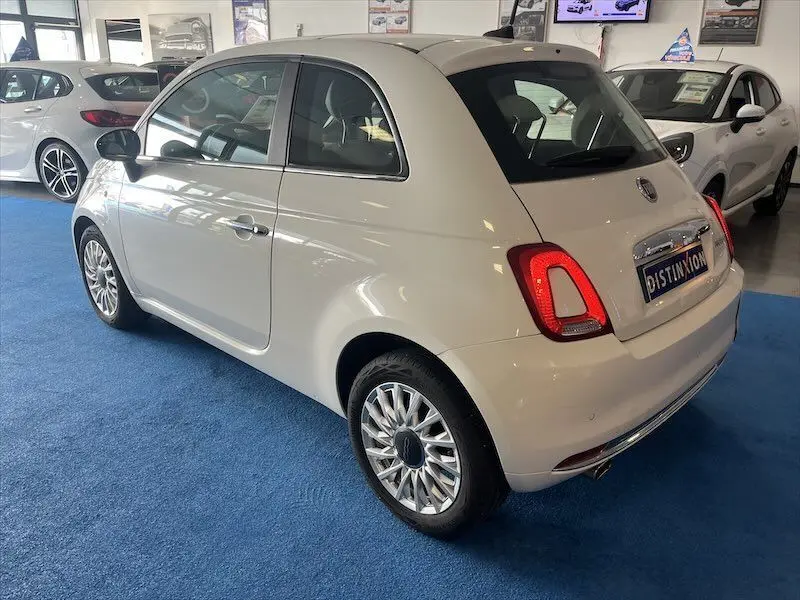 Fiat 500 blanche vue 3/4 arrière droit en intérieur, avec jantes alliage et feux arrière allumés.