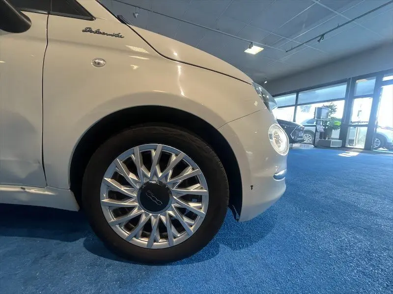 Gros plan sur la roue avant gauche et l'aile blanche d'une FIAT 500 Dolcevita dans un showroom lumineux.
