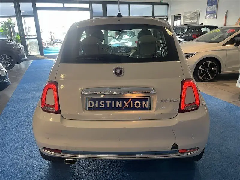 Vue arrière d'une FIAT 500 blanche hybride exposée en showroom avec feux arrière allumés et plaque Distinxion.