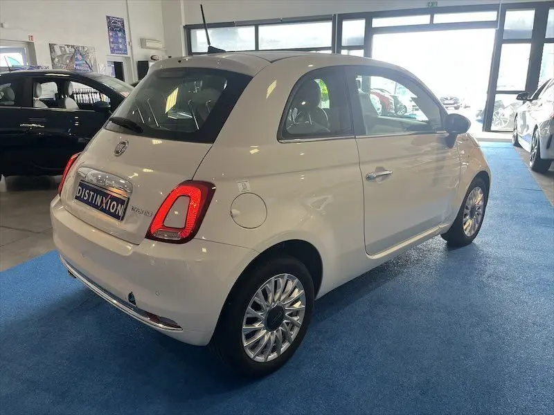 Fiat 500 blanche vue en 3/4 arrière droit dans un showroom, avec jantes alliage et feux arrière allumés.