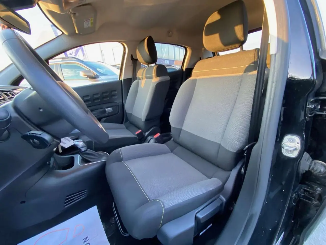 Vue intérieure côté conducteur de la Citroën C3 Shine 2023 noir toit rouge, sièges tissu gris et noir.