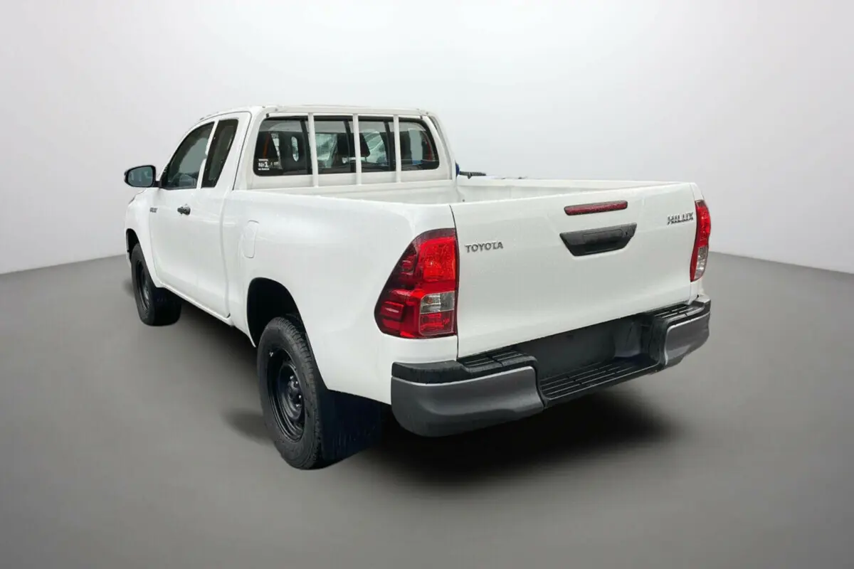 Vue 3/4 arrière d'un Toyota Hilux 4x4 blanc pur 2024 avec benne ouverte et jantes acier noires.