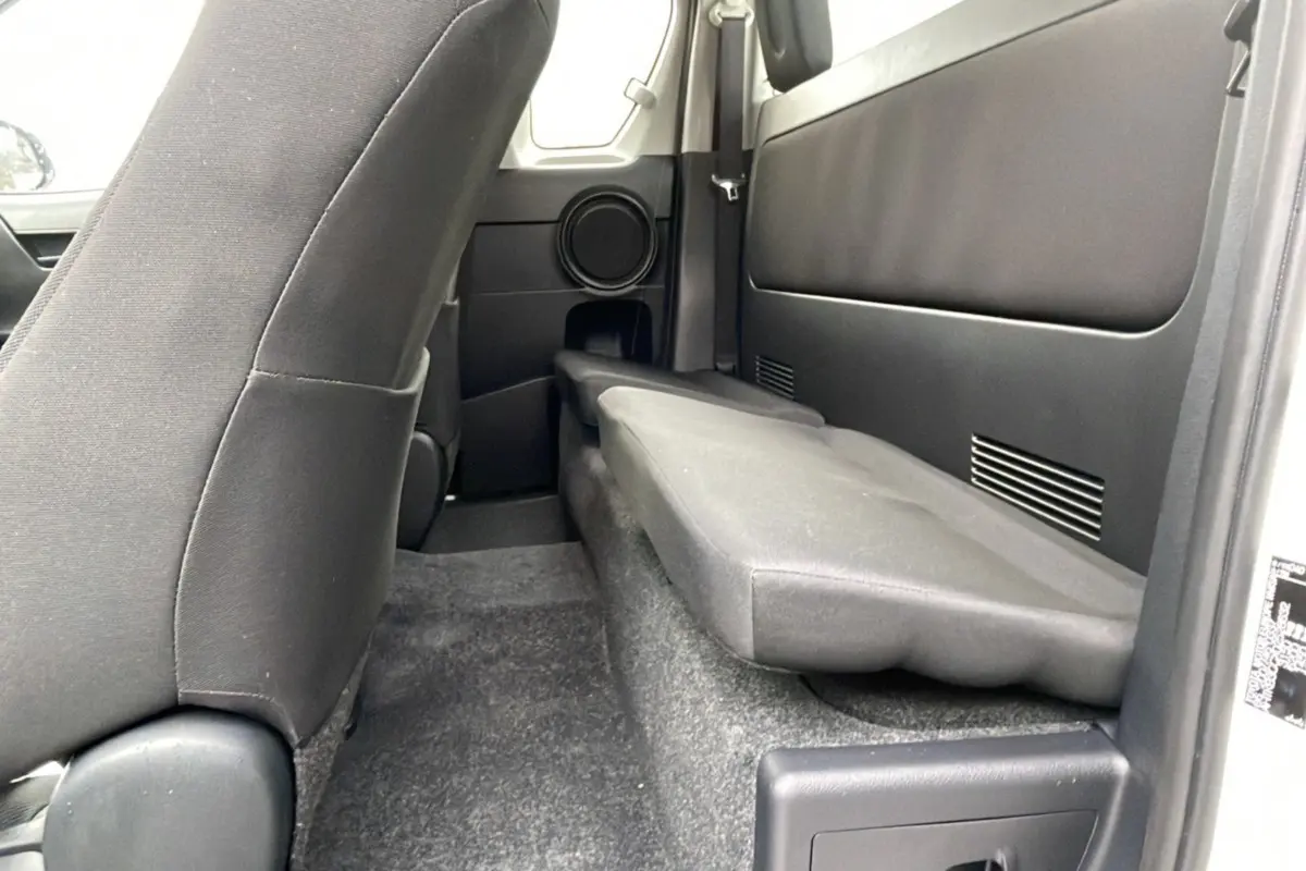 Vue intérieure côté droit du Toyota Hilux 2024 blanc, montrant la banquette arrière repliée et les sièges avant noirs.