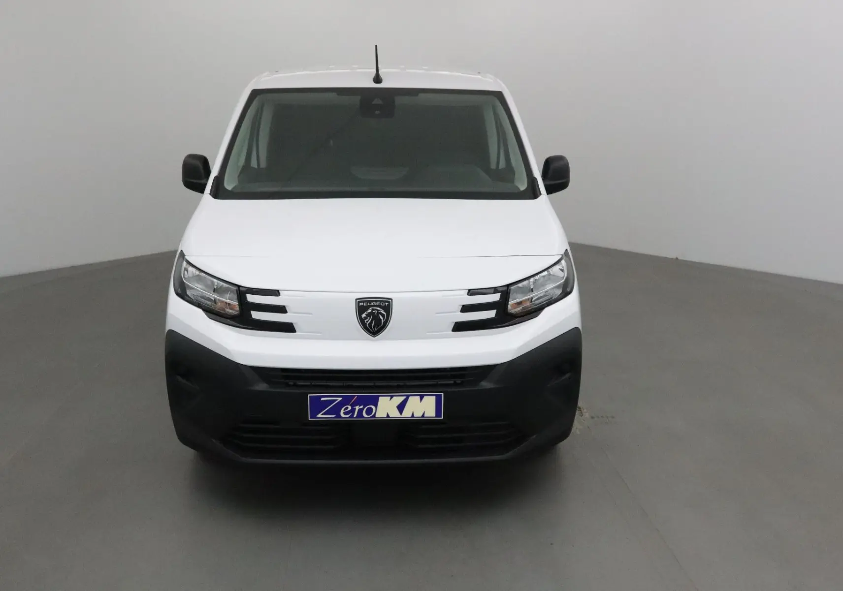 Vue de face d’un Peugeot Partner blanc 2025 avec calandre noire et logo lion central, dans un studio neutre.