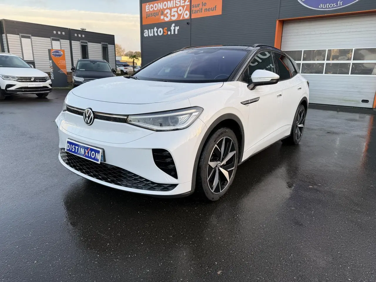 Volkswagen ID.4 GTX blanc glacier en 3/4 avant droit avec toit noir et jantes bi-colores sur parking humide.